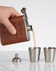 Hand pouring liquid from a leather-bound flask into metal cups, personalised in Australia. Groomsman, Bestman Proposals, wedding Gift