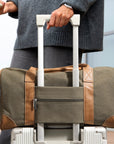 Person holding a green duffel bag with brown accents and white wheels.