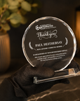 A clear crystal glass round thank-you award plaque with engraved text