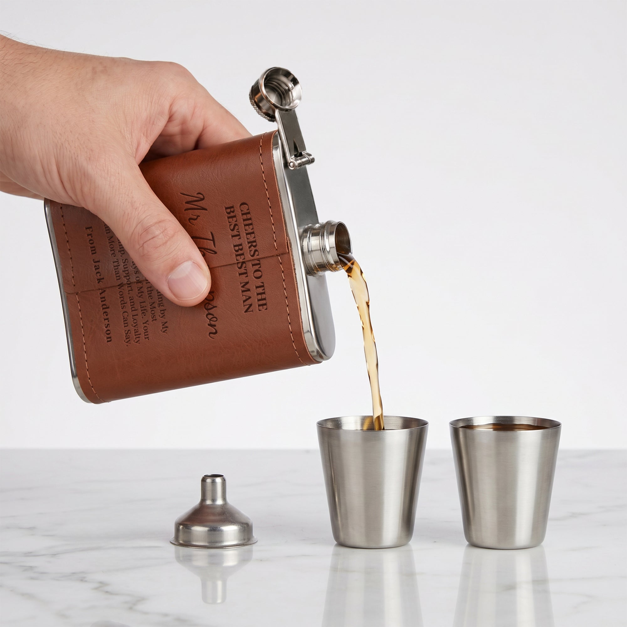 Hand pouring liquid from a leather-bound flask into metal cups, personalised in Australia. Groomsman, Bestman Proposals, wedding Gift