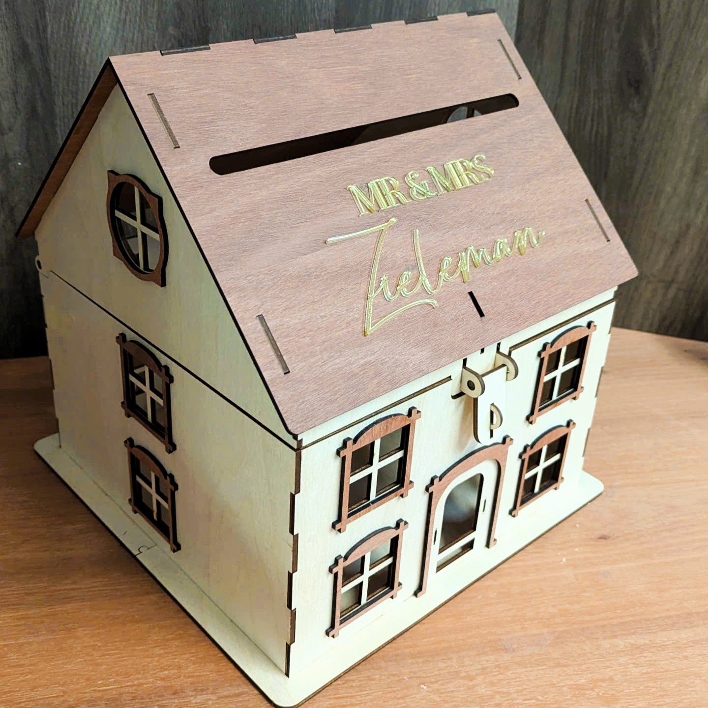 Wooden house-shaped box with &#39;Mr &amp; Mrs&#39; on the roof, placed on a wooden surface.