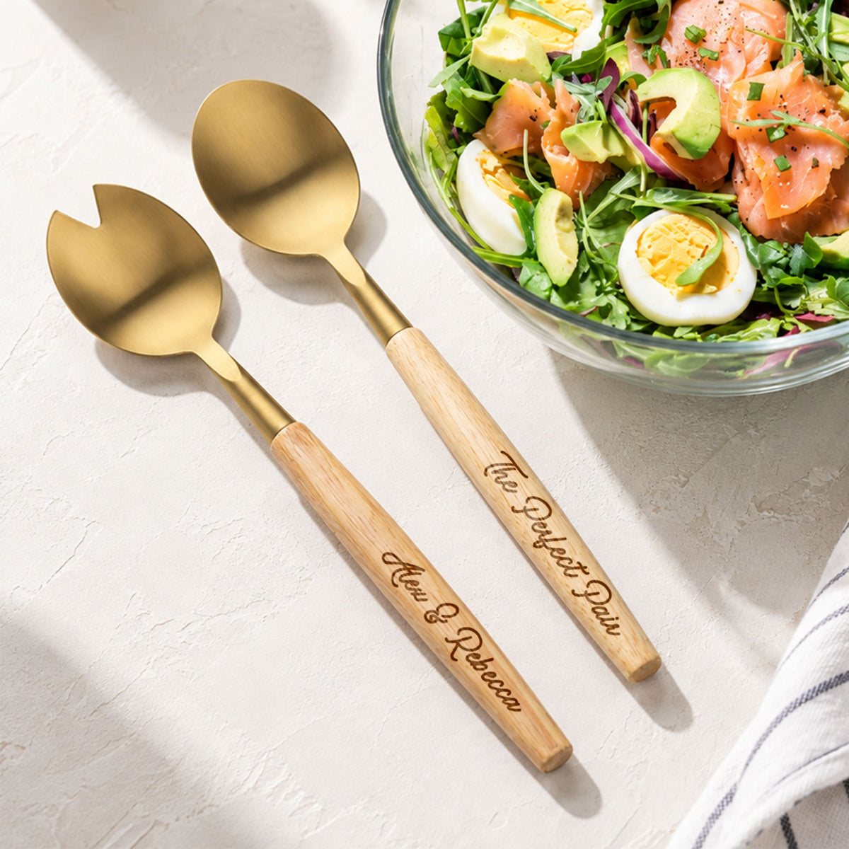 Personalised engraved acacia wood and gold salad servers beside a salad bowl