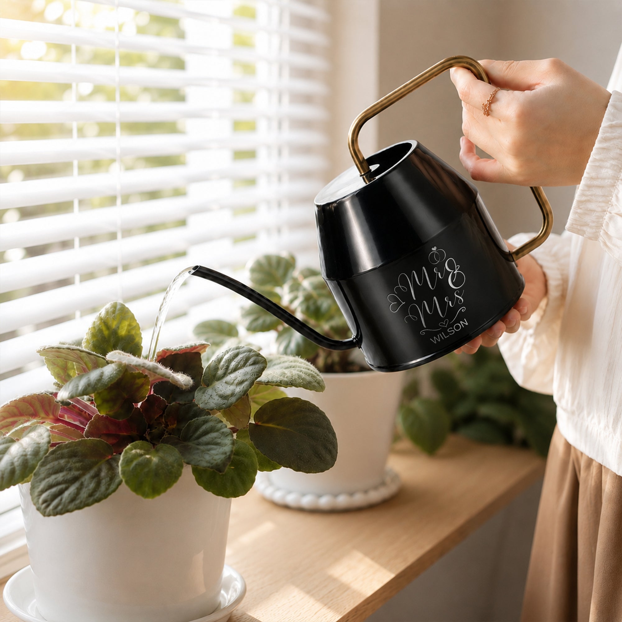 Personalised engraved black watering can with gold handle by a windowsill plant
