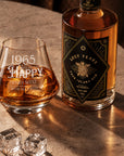 Personalised engraved whisky glass with a birthday design beside a bottle of rum