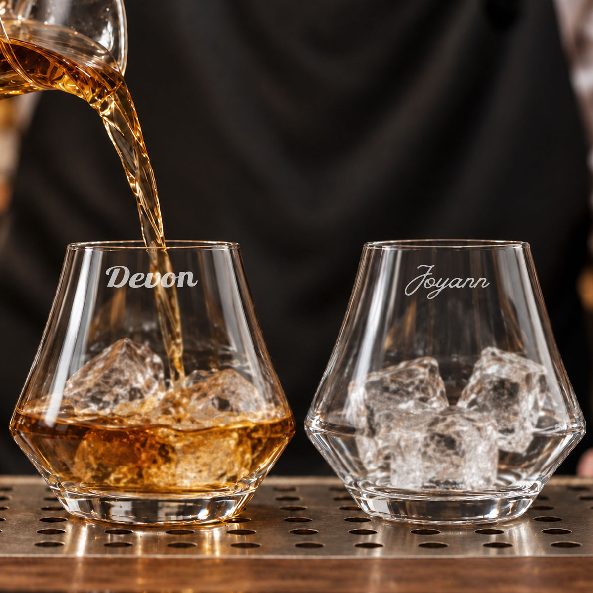 Pair of personalised whisky glasses engraved with names, whisky being poured