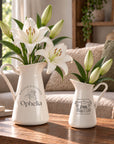 Personalised engraved white enamel vase jugs in two sizes holding lily flowers
