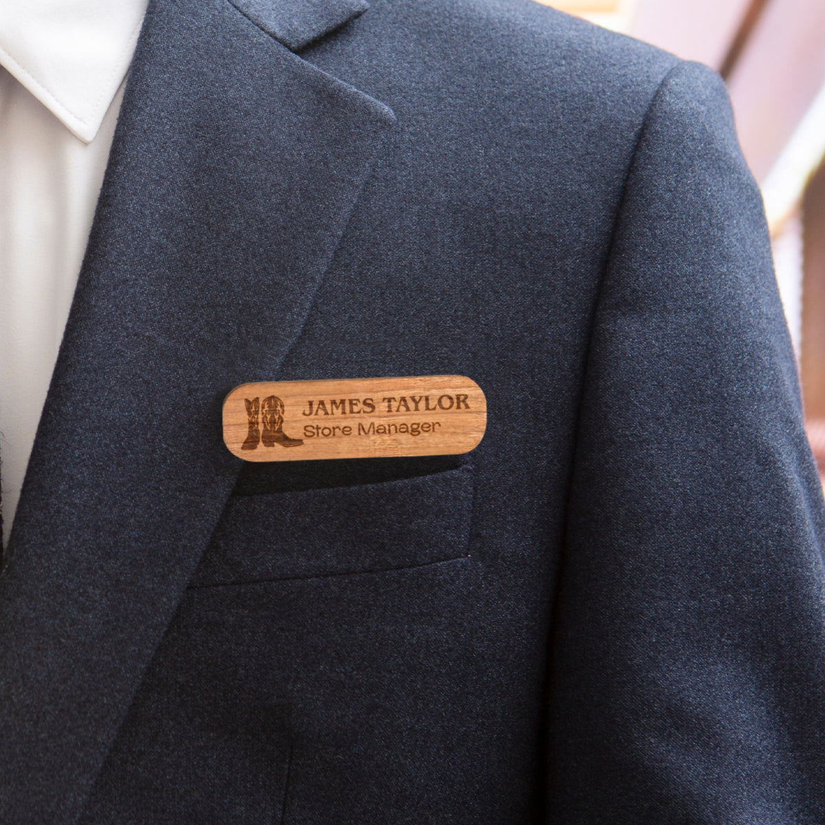 Personalised oval wooden name badge worn on a suit jacket, engraved with a name and title